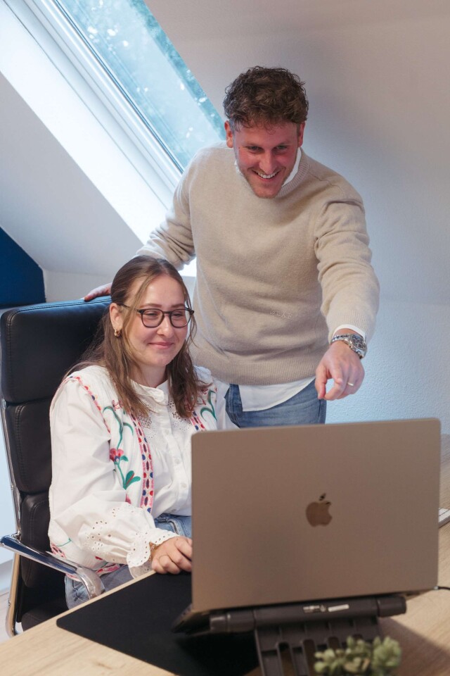 twee online markteers die samen naar een laptop kijken, waarvan er eentje naar het scherm wijst